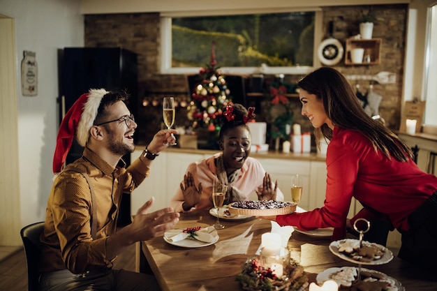 Young cheerful friends having cranberry pie for dessert while celebrating Christmas in dining room