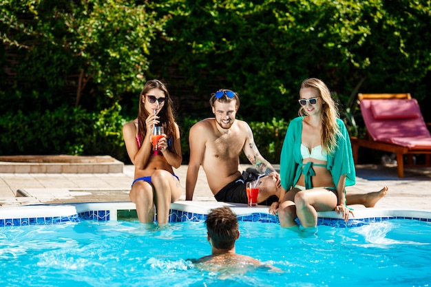 Young cheerful friends smiling, laughing, relaxing, swimming in pool