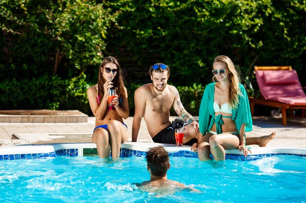 Young cheerful friends smiling, laughing, relaxing, swimming in pool