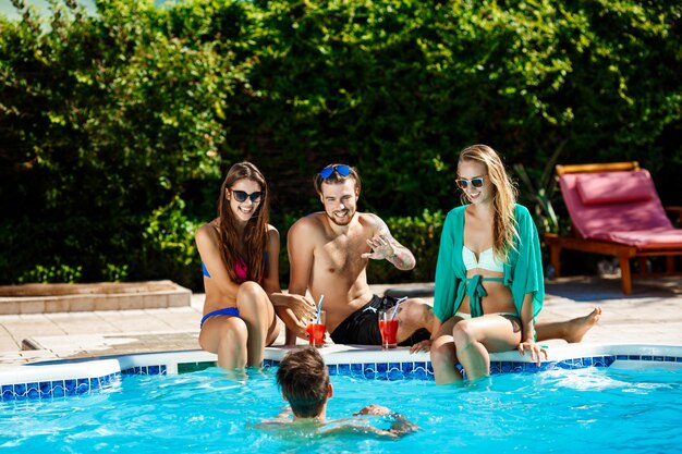 Young cheerful friends smiling, laughing, relaxing, swimming in pool