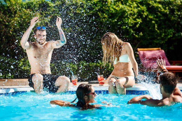 Young cheerful friends smiling, laughing, relaxing, swimming in pool