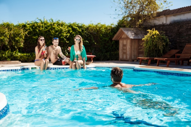 Young cheerful friends smiling, laughing, relaxing, swimming in pool