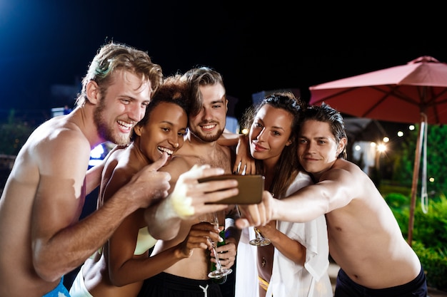 Young cheerful friends smiling, rejoicing, making selfie, resting at party