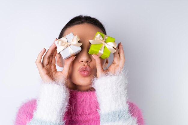 Young cheerful girl in a soft colored sweater on a white background holds small cute gift boxes