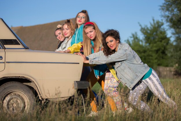 Молодые веселые девушки толкают старую машину женщины в стиле 90-х