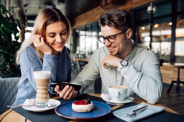 Young cheerful guy and girl in headphones, watching a movie on mobile phone