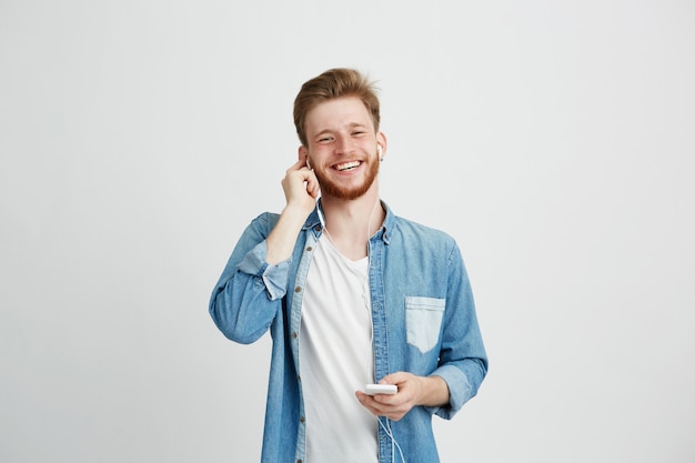 Young cheerful guy in headphones smiling holding phone listening to music.