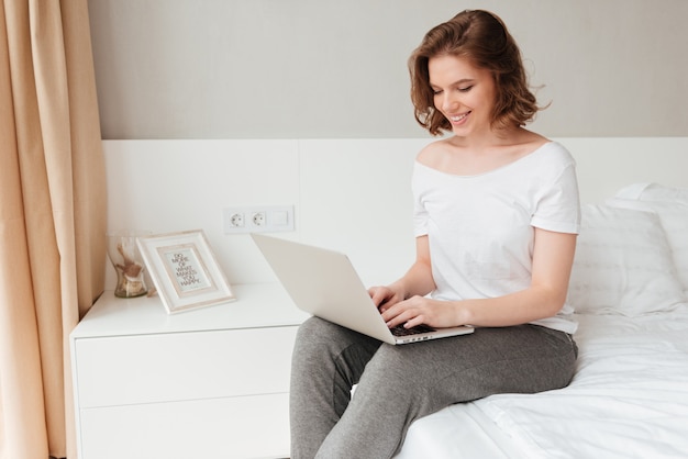 Young cheerful lady sitting indoors using laptop computer