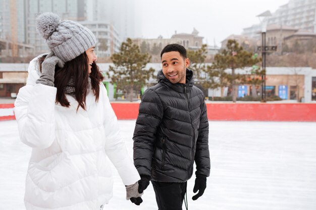 Young cheerful loving couple skating at ice rink outdoors