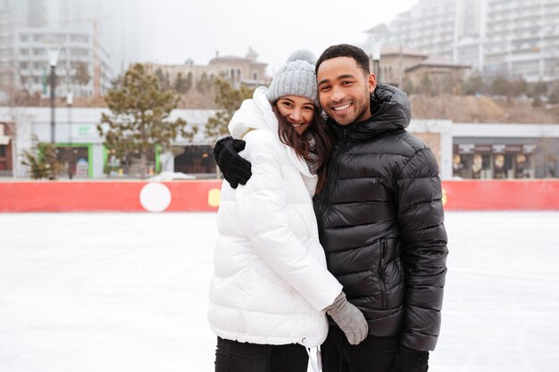 Young cheerful loving couple skating at ice rink outdoors.