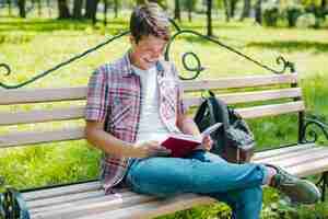 Free photo young cheerful man reading book in park