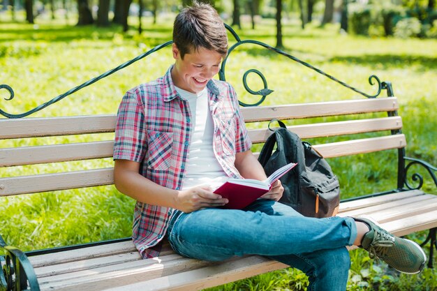 Young cheerful man reading book in park
