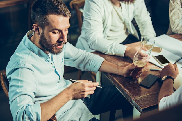 Young cheerful people smile and gesture while relaxing in pub.