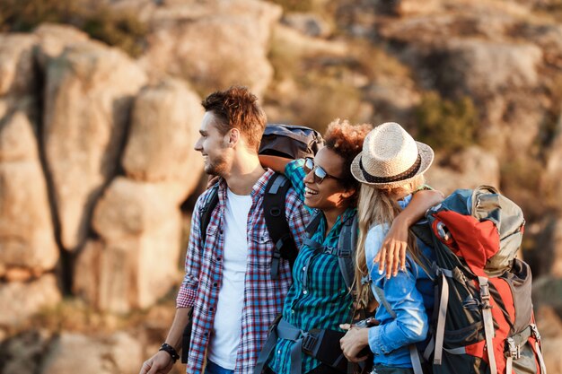 Young cheerful travelers with backpacks smiling, embracing, walking in canyon