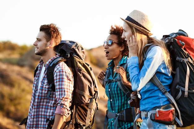 Foto gratuita giovani viaggiatori allegri con zaini sorpresi, sorridenti, che camminano nel canyon