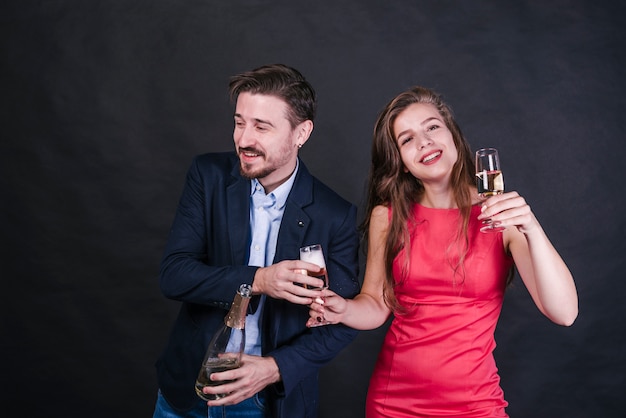 Free photo young cheerful woman giving glass of drink to man with bottle of champagne