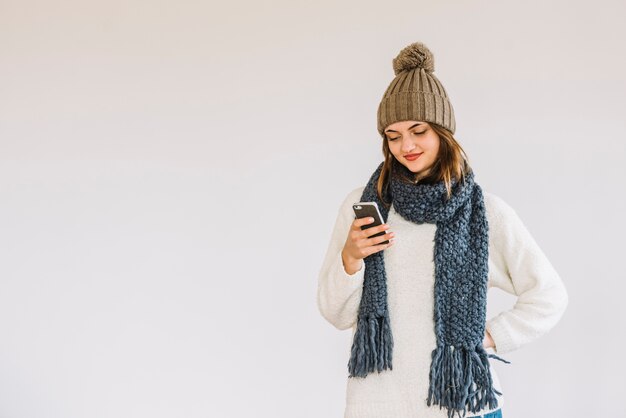 Young cheerful woman in hat and scarf with smartphone