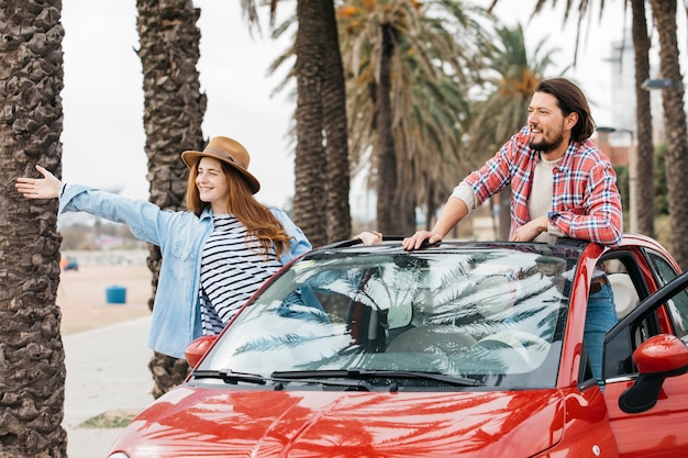 Young cheerful woman and man leaning out from car