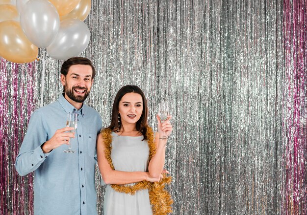 Young cheerful woman near handsome man with glasses near tinsel and balloons 