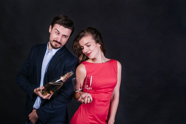 Young cheerful woman near man with bottle of drink pouring glasses