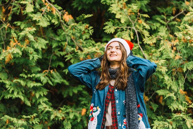 Young cheerful woman in party hat near coniferous branches