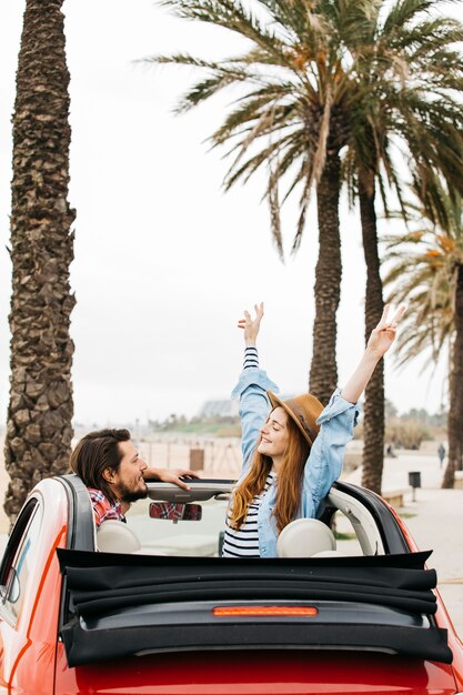 Young cheerful woman with upped hands and man leaning out from car