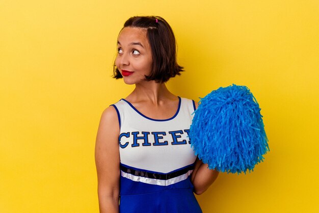Young cheerleader mixed race woman isolated on yellow background looks aside smiling, cheerful and pleasant.