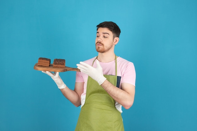 Young chef holding fresh chocolate cake slices .