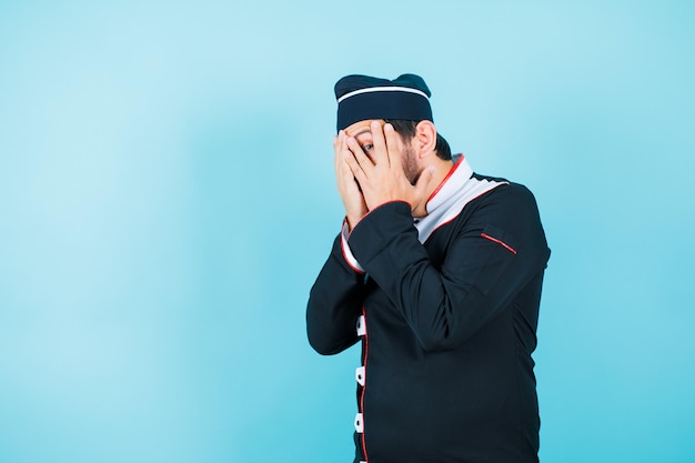 Young chef is peeking through fingers on blue background