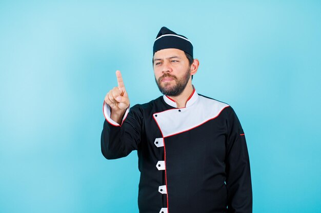 Young chef is pointing away with forefinger on blue background