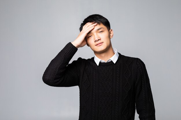 흰 벽에 고립 된 두통을 입고 젊은 중국 남자. 스트레스와 과로의 개념.