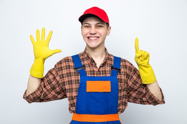 Young cleaning guy wearing uniform and cap with gloves isolated on white wall