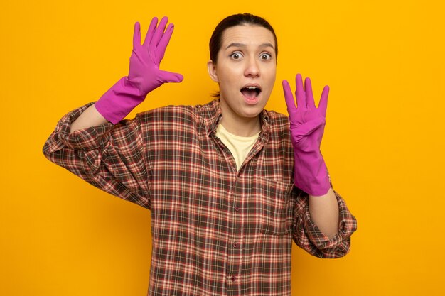 Молодая уборщица в клетчатой рубашке в резиновых перчатках изумлена и удивлена, показывая номер девять с пальцами, стоящими на оранжевом