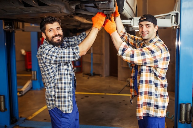 Young colleagues looking at the camera while repairing car tire in the service center