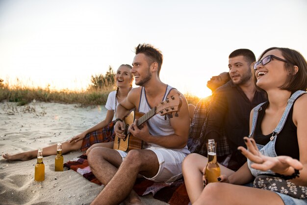 Молодая компания друзей, радуясь, отдыхая на пляже во время восхода солнца