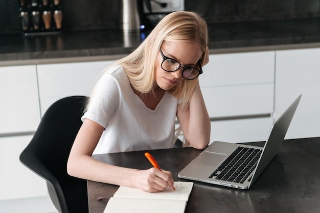 Young concentrated lady working at home with laptop and notebook