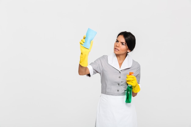 Young concentrated maid in uniform cleaning window with rag