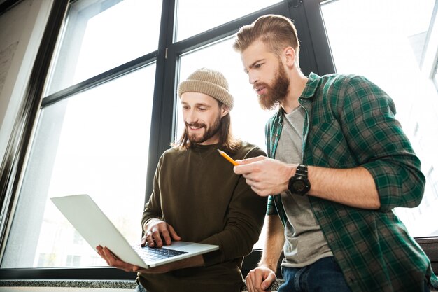 Young concentrated men colleagues in office using laptop