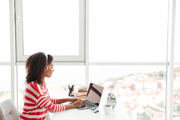 Free photo young confident african woman in headphones working on laptop