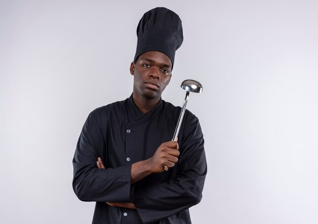 Young confident afro-american cook in chef uniform crosses arms holds ladle on white  with copy space