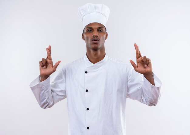 シェフの制服を着た若い自信を持ってアフリカ系アメリカ人の料理人は、コピースペースで白い背景で隔離の両手の指を交差させます