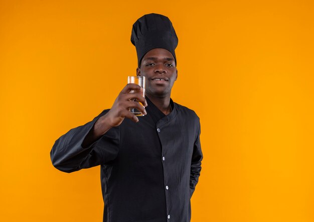 요리사 제복을 입은 젊은 자신감 아프리카 계 미국인 요리사는 복사 공간이있는 오렌지에 물 한 잔을 보유하고 있습니다.