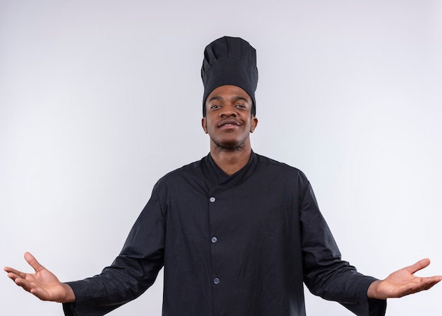 Молодой уверенный афро-американский повар в униформе шеф-повара держит руки открытыми на белом фоне с копией пространства