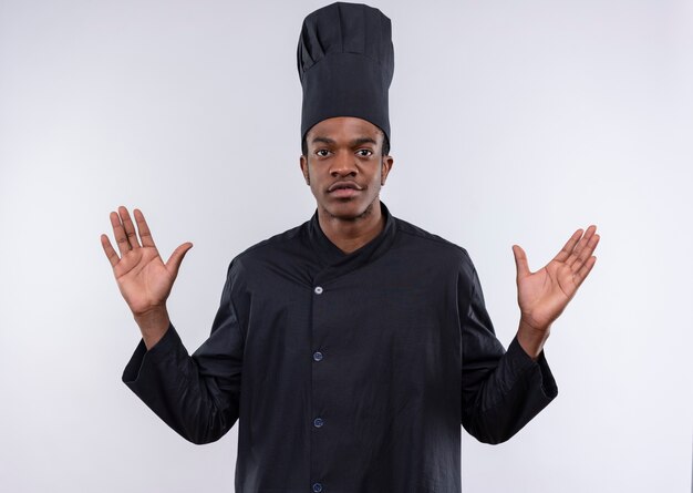 Young confident afro-american cook in chef uniform holds hands up isolated on white background with copy space