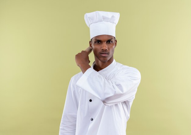 요리사 제복을 입은 젊은 자신감 아프리카 계 미국인 요리사는 복사 공간이 녹색 배경에 고립 된 손으로 뒤에 롤링 핀을 보유하고 있습니다.
