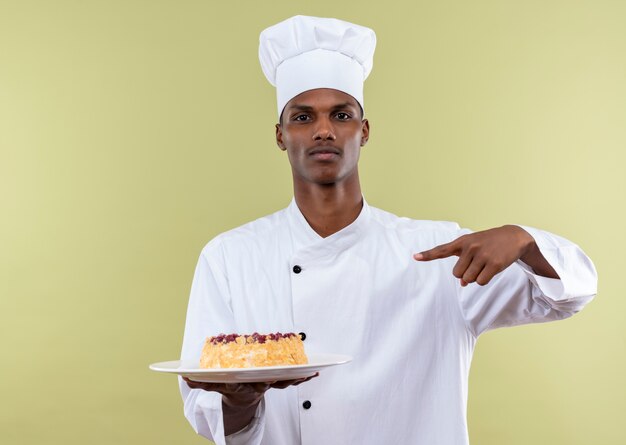 복사 공간 녹색 배경에 고립 접시에 케이크에 요리사 유니폼 포인트에서 젊은 자신감 아프리카 계 미국인 요리사