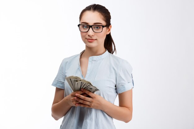 Young confident beautiful business girl in glasses holding money over white wall