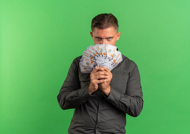 Free photo young confident blonde handsome man holds and looks over money isolated on green space with copy space