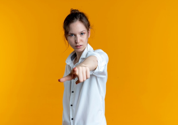 Free photo young confident blonde russian girl points at camera isolated on orange space with copy space