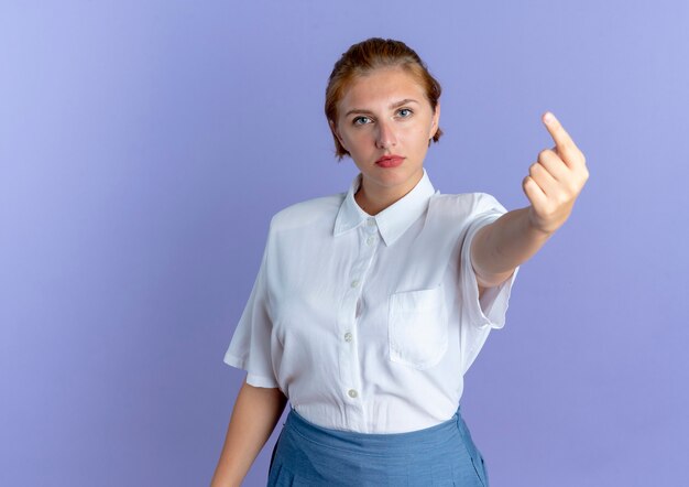 Молодая уверенная русская блондинка показывает указательный палец на фиолетовом фоне с копией пространства